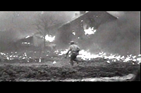 infantryman in open field with burning house